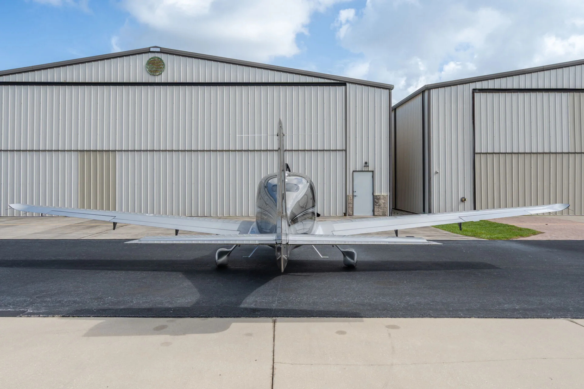 Rear view of a silver Cirrus SR22T aircraft (N3404) parked on an airport tarmac in front of hangars.