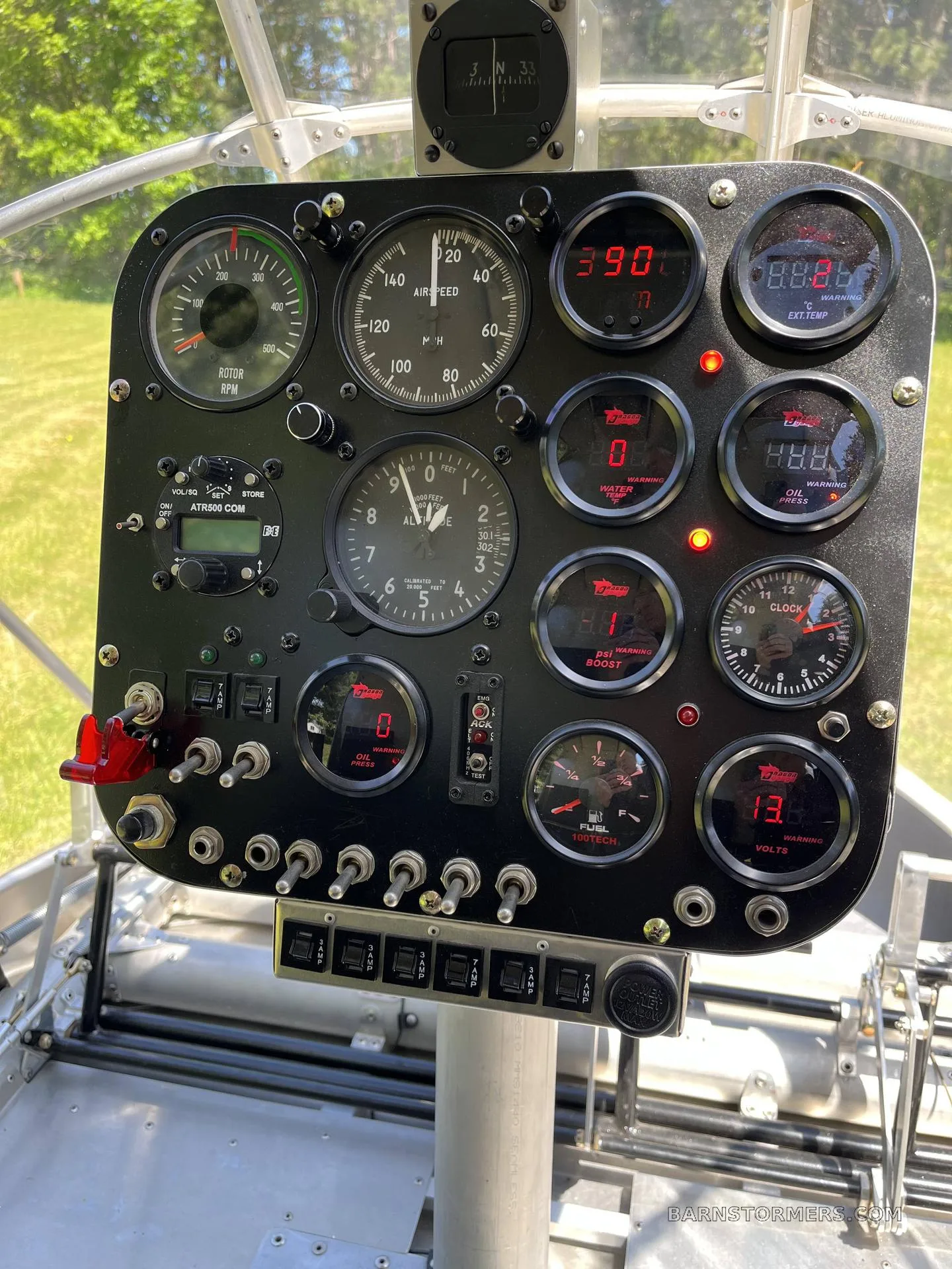 A close-up view of a black instrument panel with various analog and digital gauges, switches, and a radio.