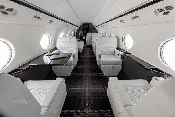 The luxurious interior cabin of a private jet, featuring white leather seats and a dark plaid carpet.