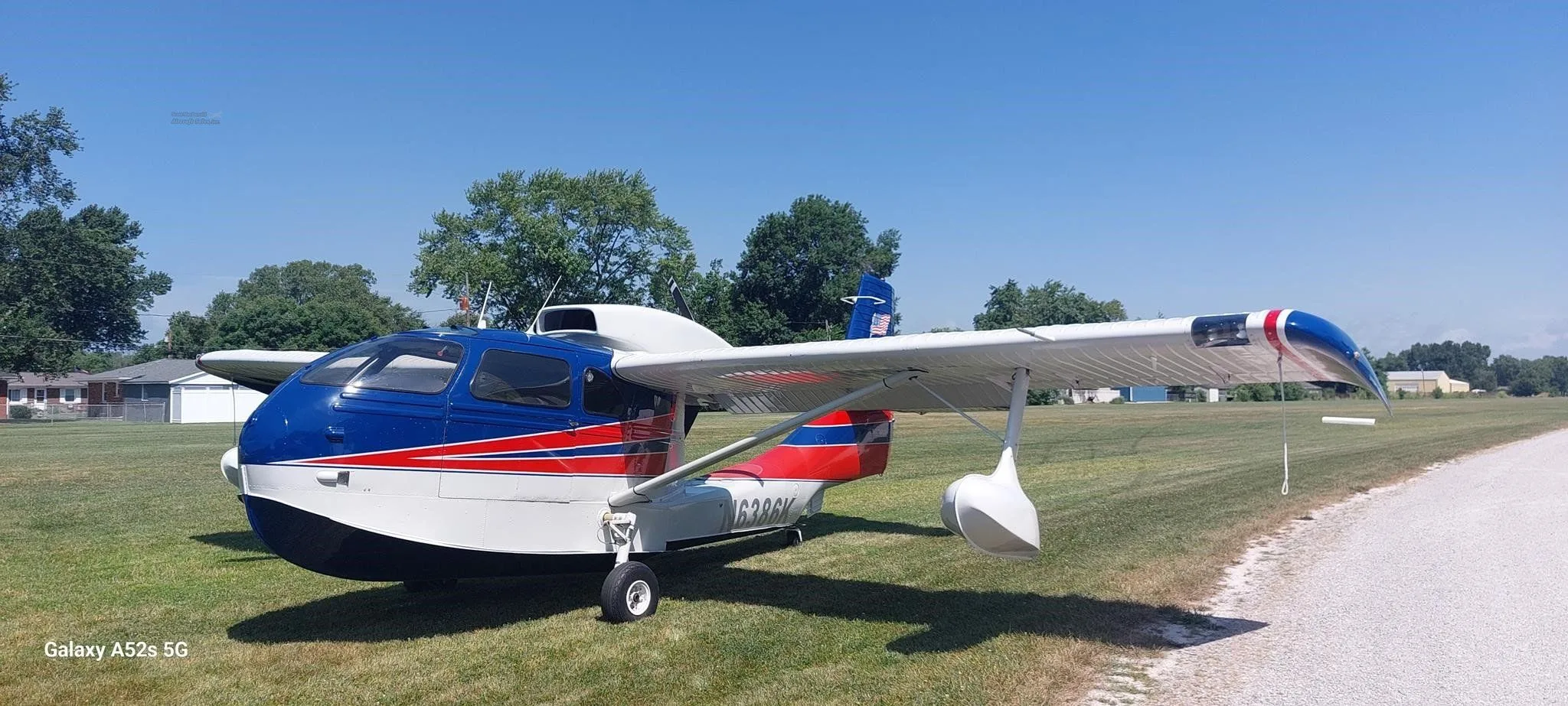 A blue, white, and red amphibious aircraft with registration N6386K parked on a grassy field under a clear sky.