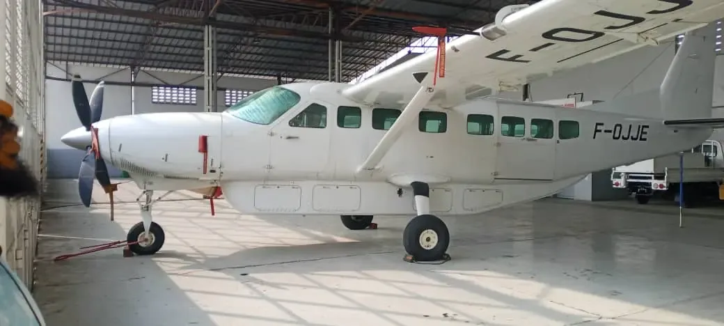 A white Cessna 208 Caravan aircraft with registration F-OJJE is parked inside a hangar, viewed from the front right.