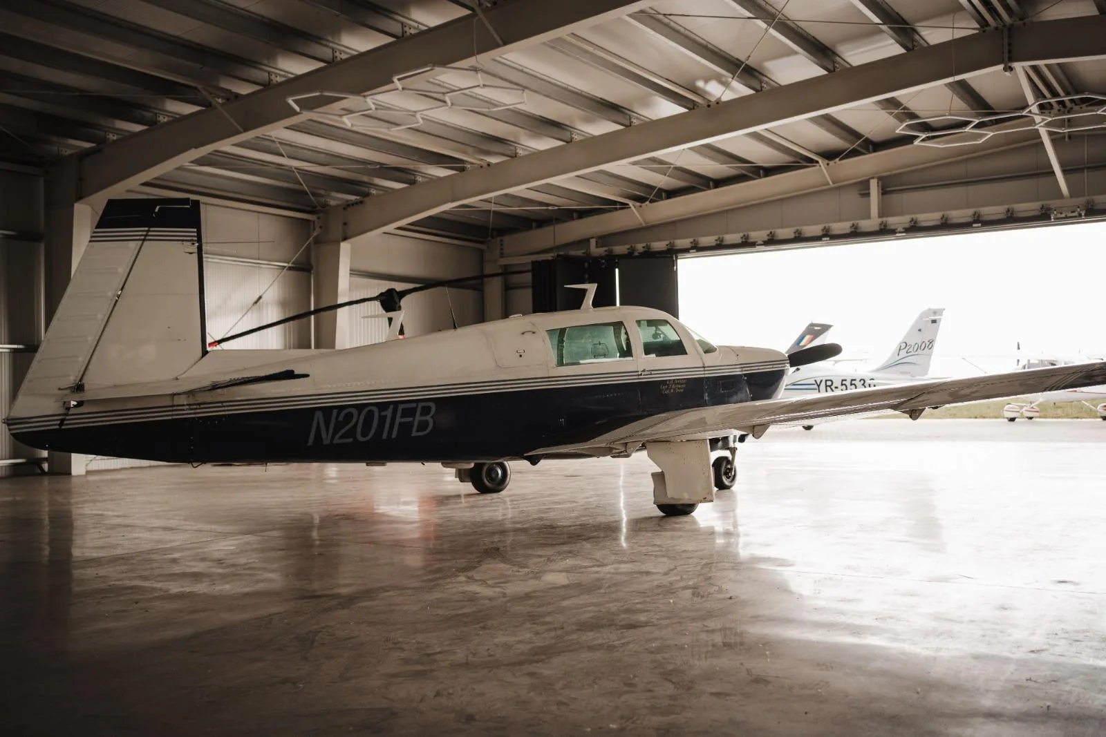 A rear-left view of the N201FB single-engine aircraft parked inside a hangar.