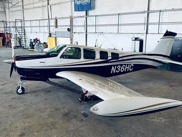 A dark blue and white Beechcraft Bonanza N36HC with gold stripes is parked in a hangar.