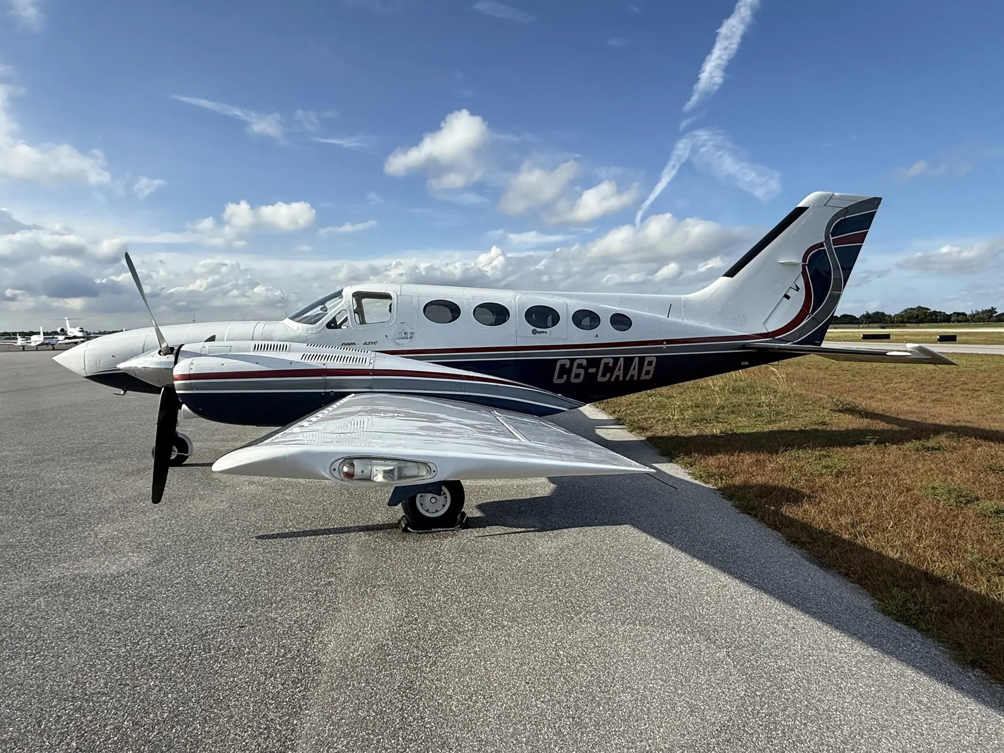 A white and blue Cessna 414 Chancellor twin-engine aircraft with registration C6-CAAB parked on an asphalt tarmac under a blue sky.