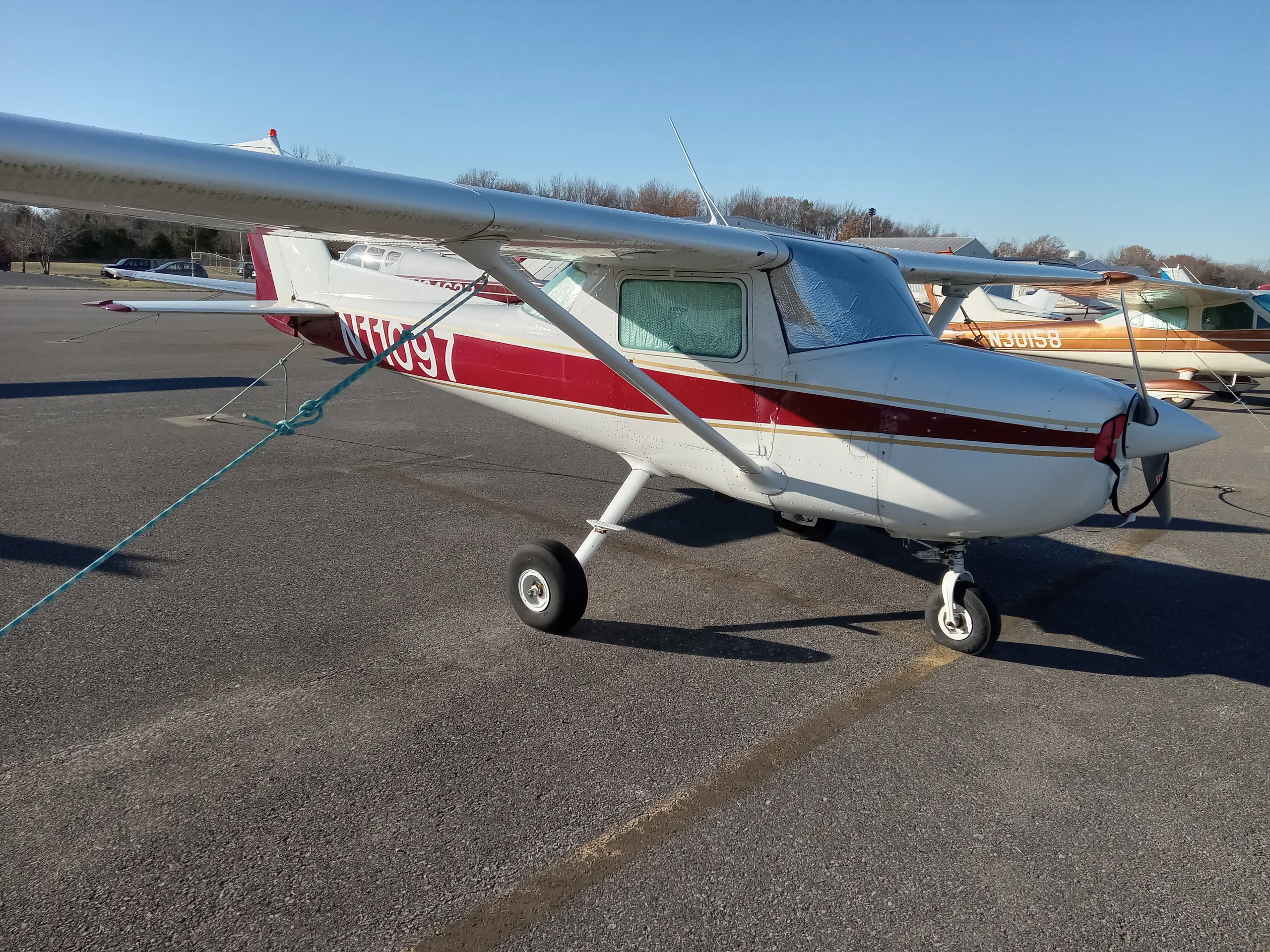 A white and maroon Cessna 150 or 152 aircraft, N11097, parked on an asphalt ramp on a sunny day.