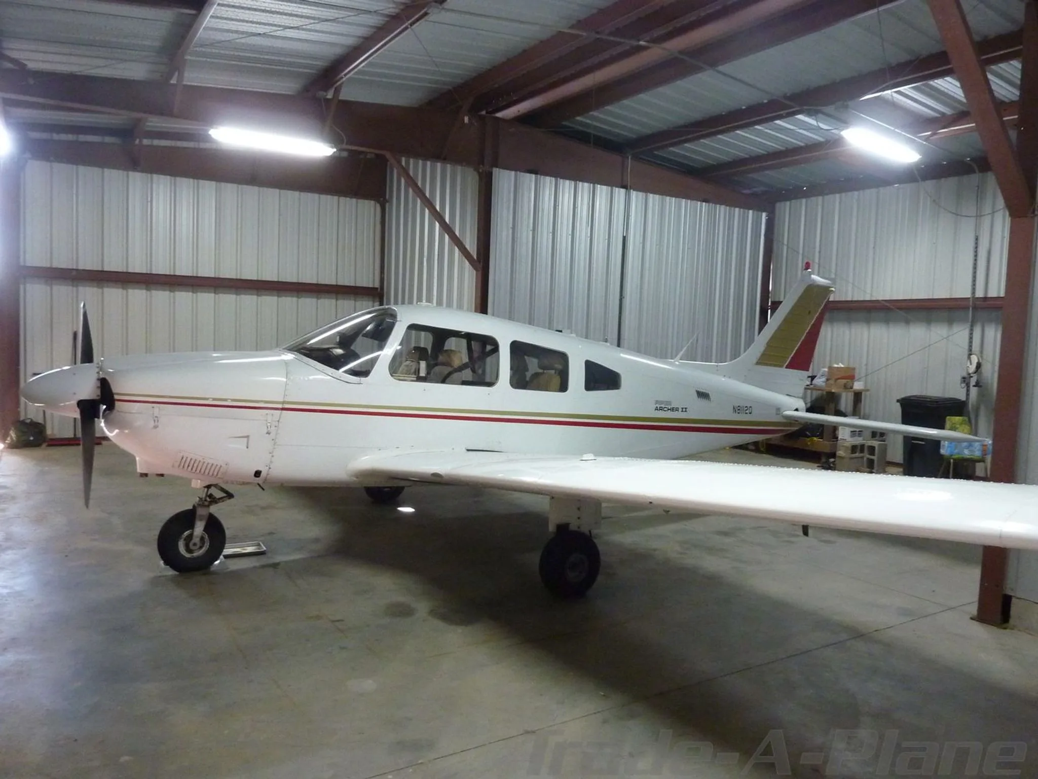 A white Piper Archer II aircraft with red and gold stripes, registration N8112Q, parked inside a hangar.