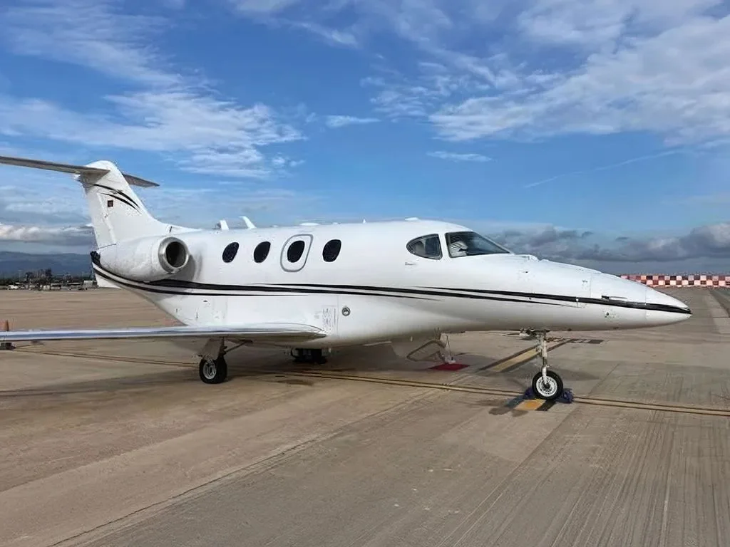 A white business jet with black stripes parked on an airport tarmac under a partly cloudy sky.