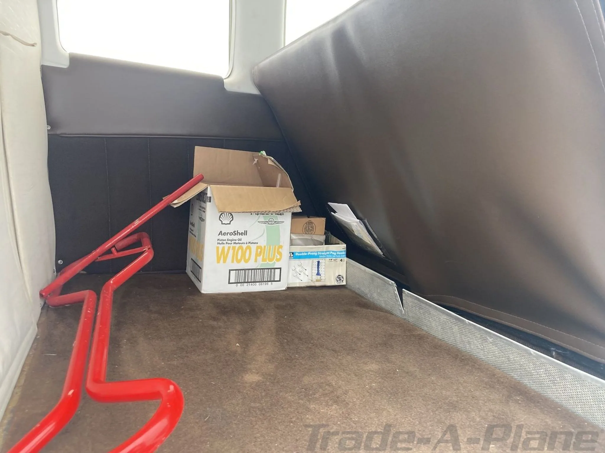 The aircraft's baggage compartment with a box of AeroShell engine oil and a red tow bar.