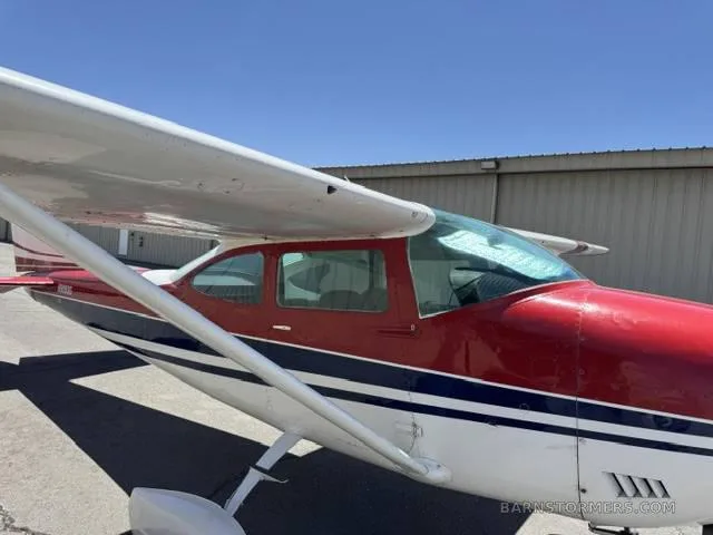 A red, white, and blue single-engine propeller aircraft parked on an asphalt ramp next to a hangar.