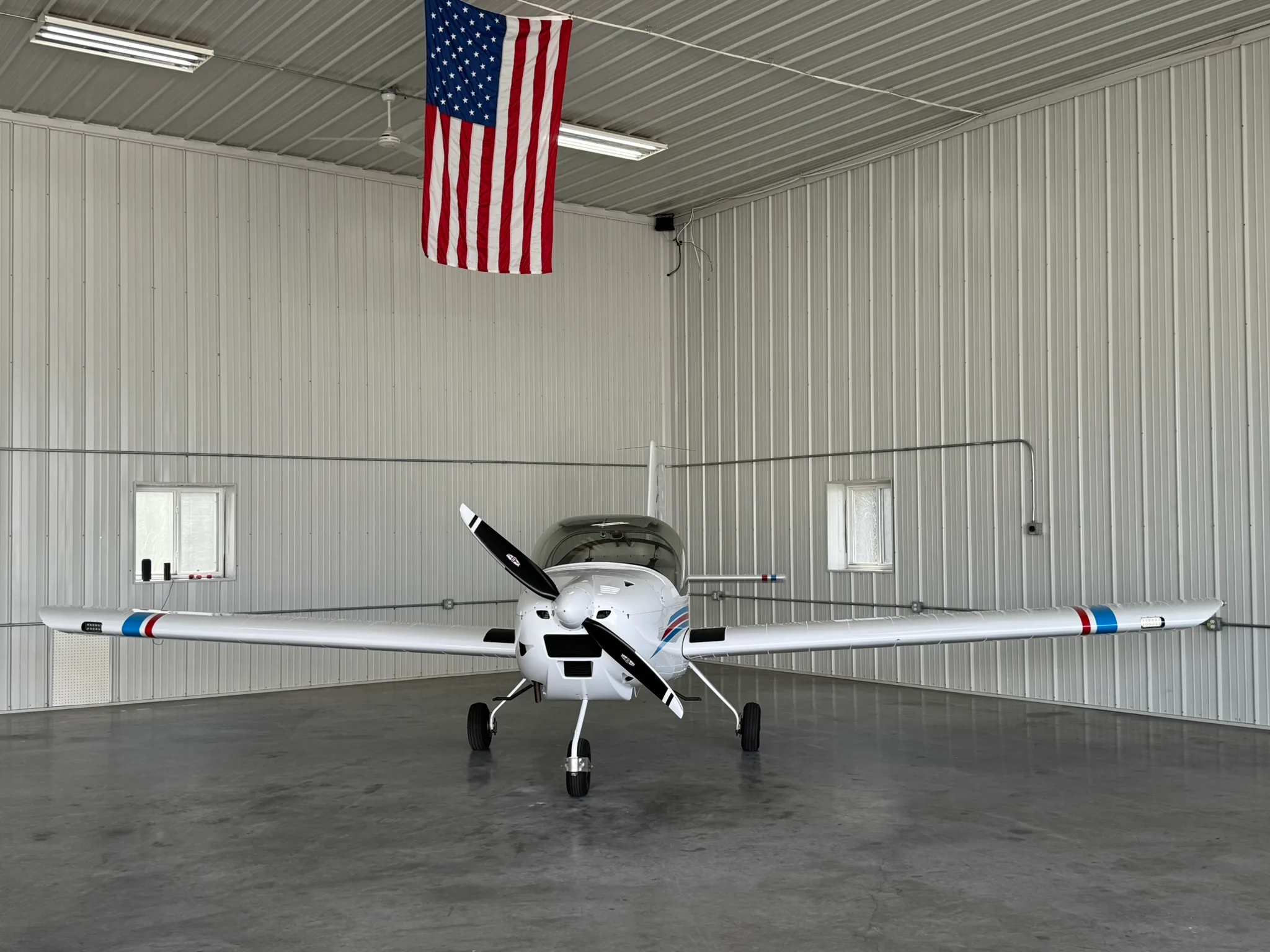 A white Van's RV-12iS aircraft with red and blue wingtip stripes, viewed from the front in a hangar.