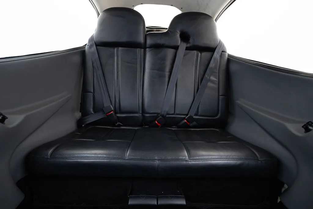 View of the black leather rear bench seat with two seatbelts in the aircraft cabin.