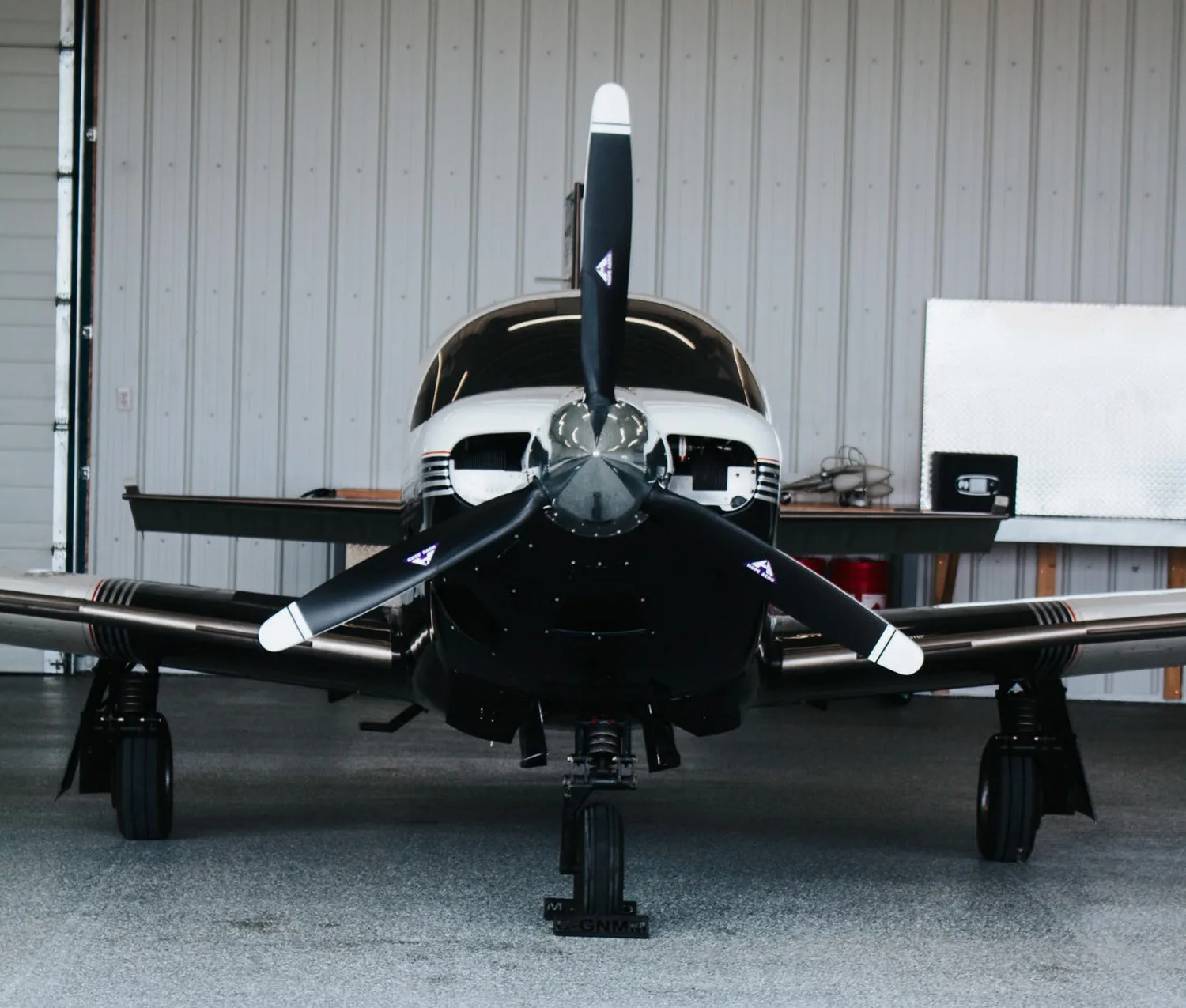 A black and white single-engine propeller aircraft is parked head-on inside a hangar.