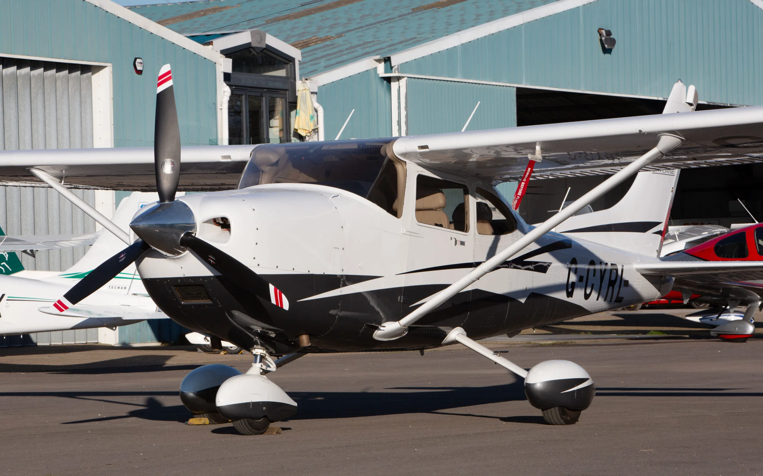 A white and black Cessna 182T (G-CYRL) parked on an airfield in front of a hangar.