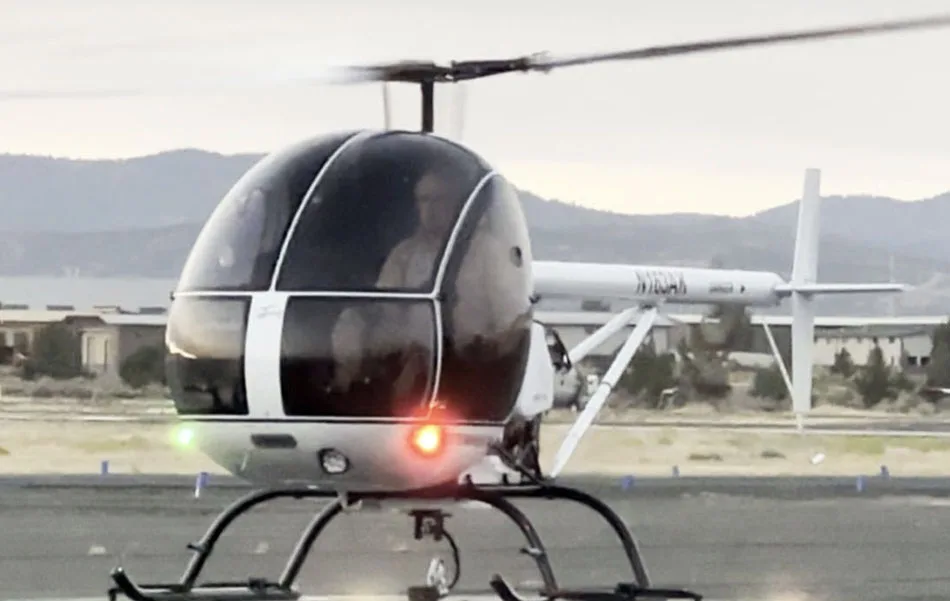 A white and black helicopter, N162JS, with its rotor spinning, on a landing pad with mountains in the background.