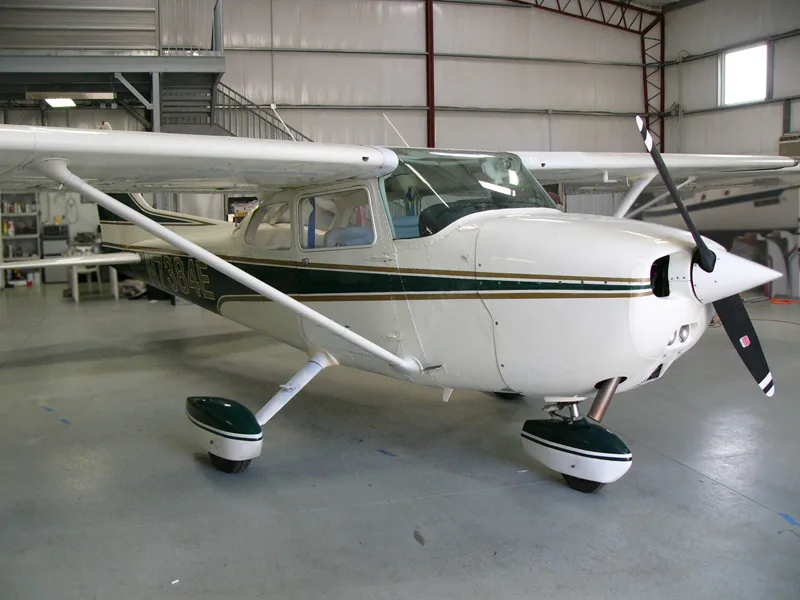 A white single-engine propeller aircraft with dark green and gold stripes, tail number N7384E, parked inside a hangar.
