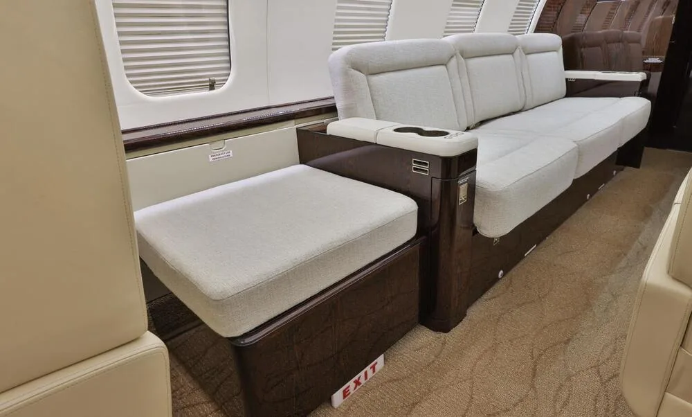 A detailed view of the private jet's cabin showing a light grey upholstered footrest and a section of the sofa.