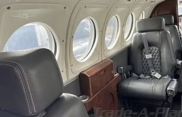 Interior view of an aircraft cabin with dark leather seats and multiple round windows.