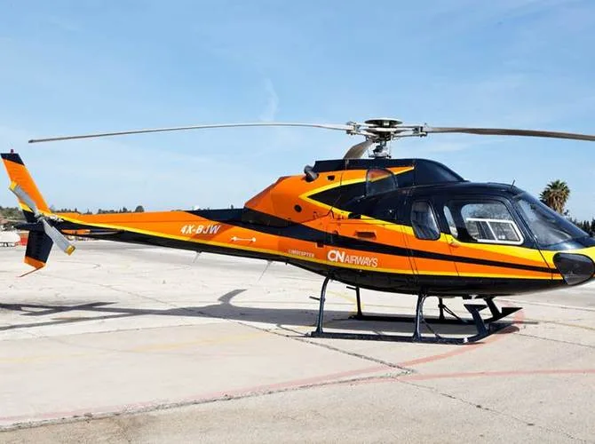 A black and orange helicopter with yellow stripes and 'CN AIRWAYS' livery, registration 4X-BJW, parked on an asphalt tarmac.