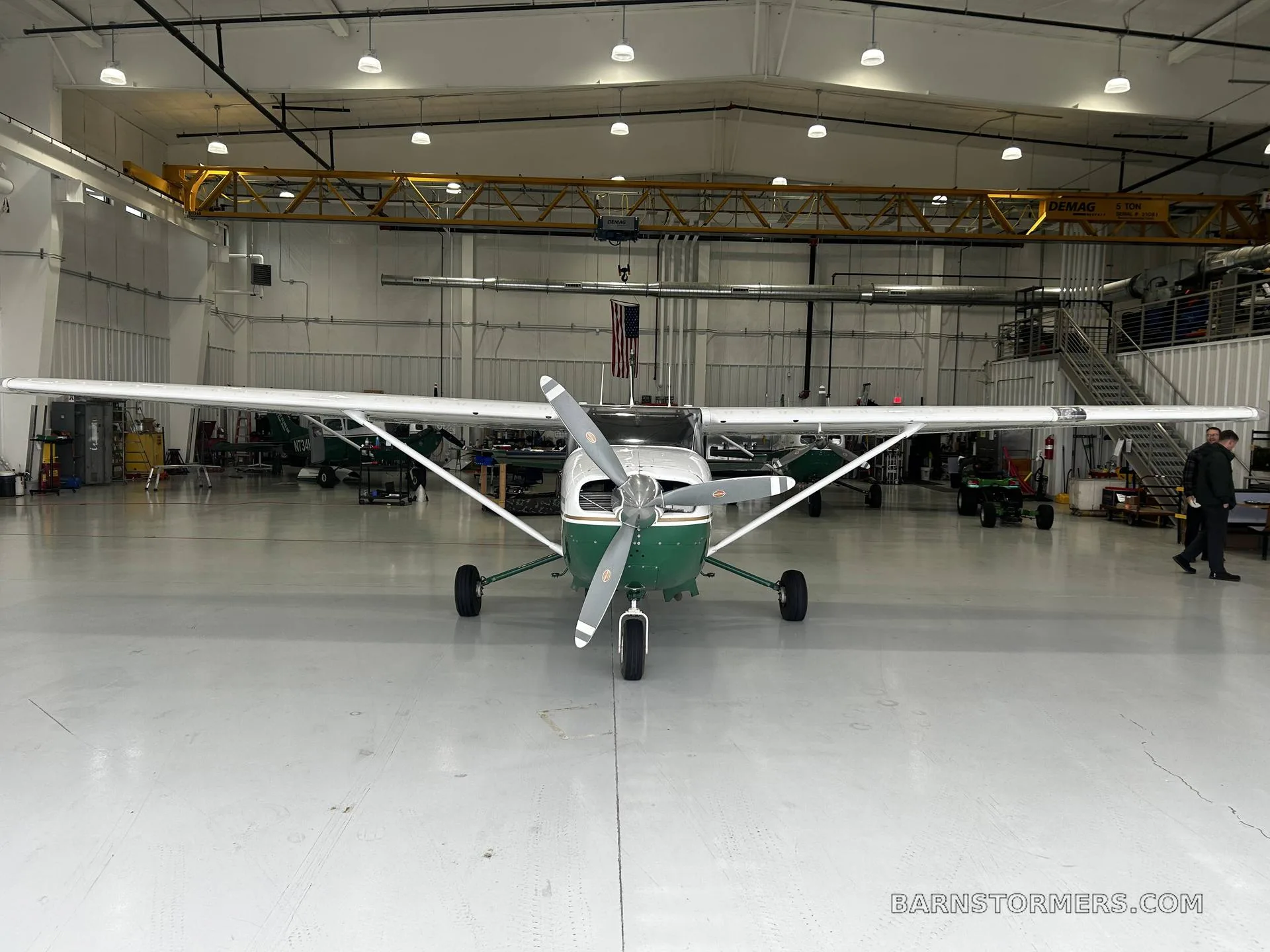A white and green Cessna 207 Stationair aircraft is parked head-on in a brightly lit hangar.