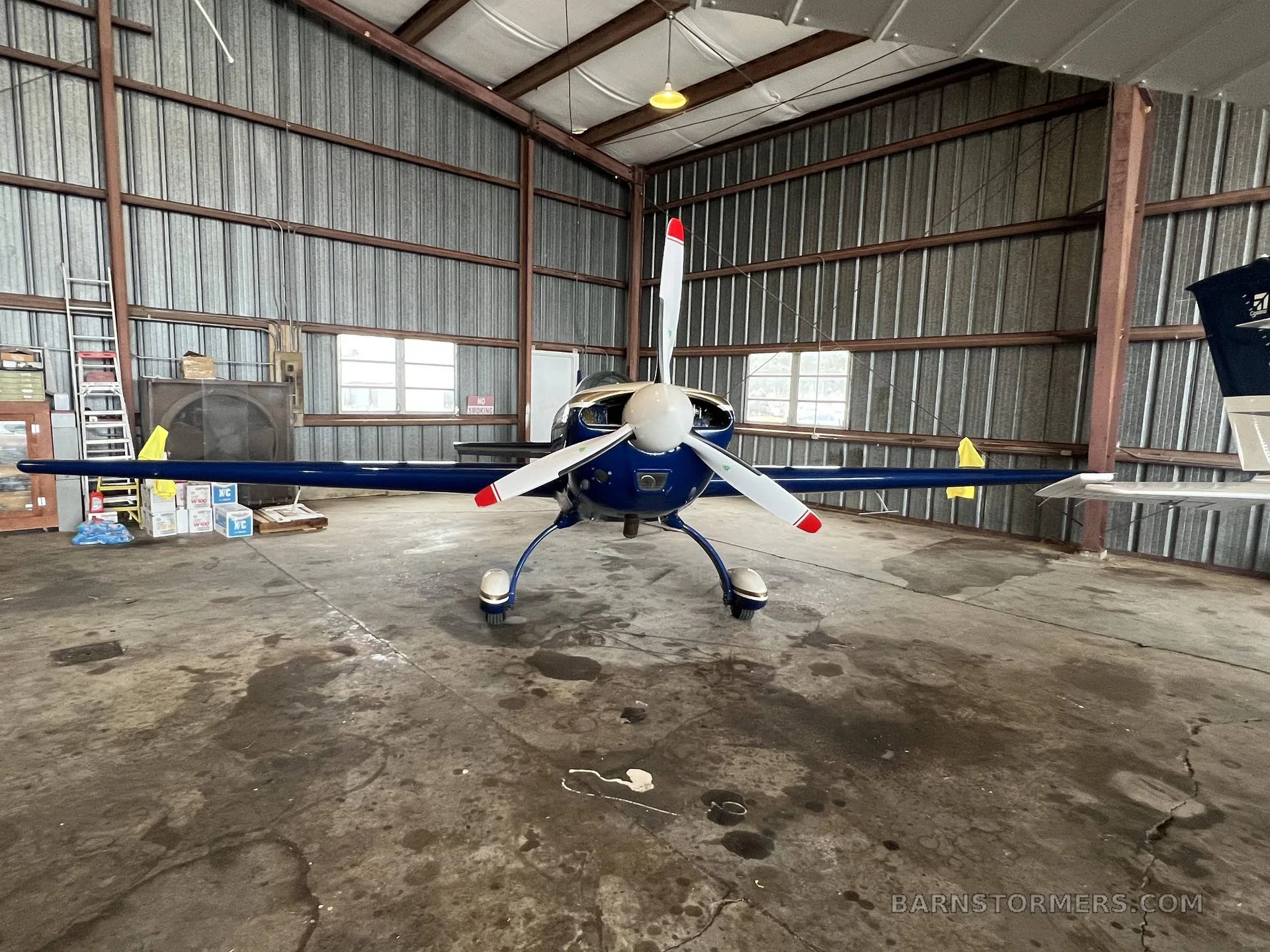 A blue and white Extra 300L aircraft with tail number N244JT is parked inside a metal hangar, viewed from the front.