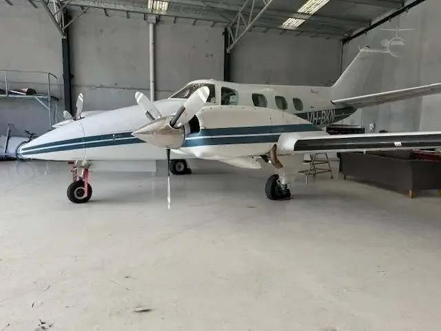 A white and blue twin-engine propeller aircraft, registration VH-BKN, is parked inside a hangar.