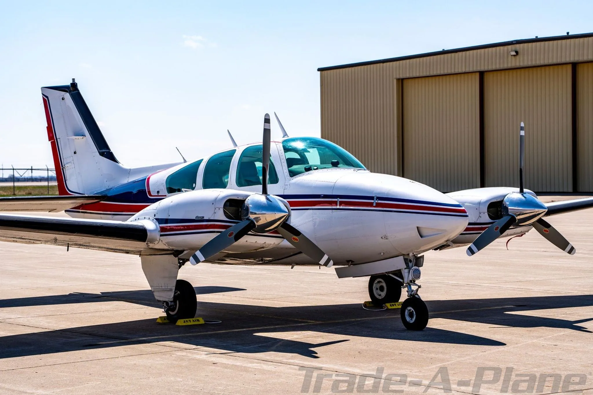 Front-right view of the N4UF twin-engine Beechcraft Baron with red and blue stripes parked near a hangar.