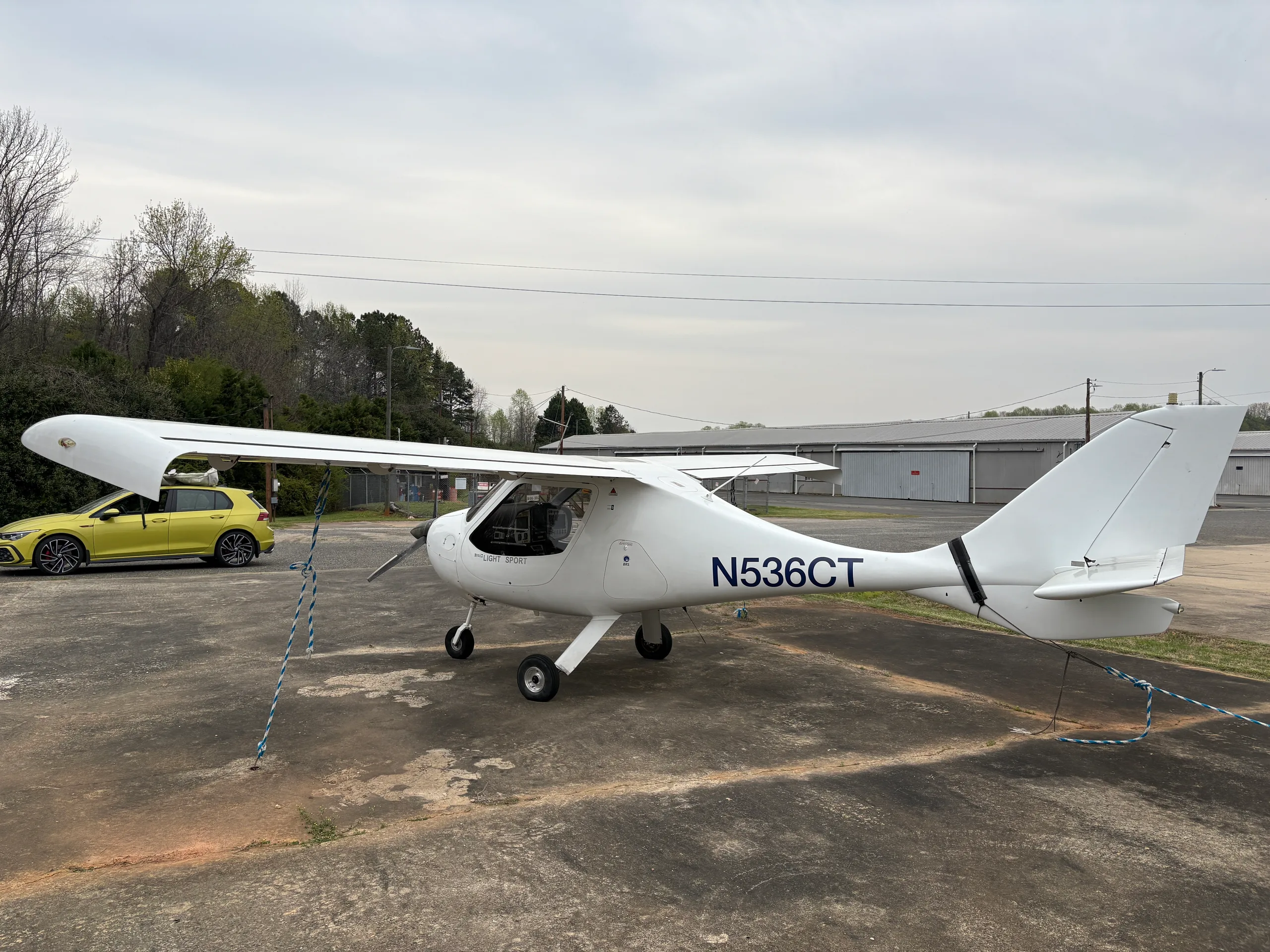 A white light sport aircraft, N536CT, is parked on a tarmac with a yellow car in the background.