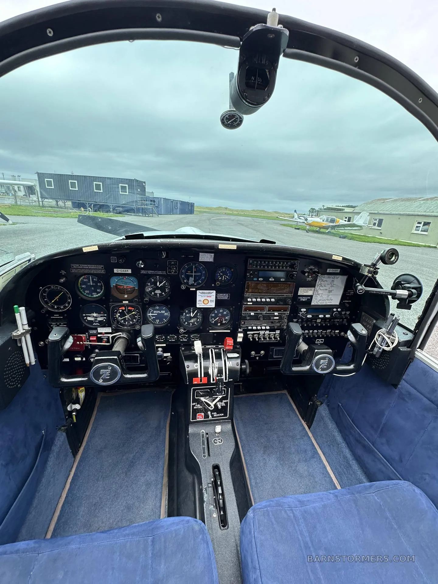 A wide view of the aircraft's cockpit, showing the instrument panel, blue seats, and the runway outside.
