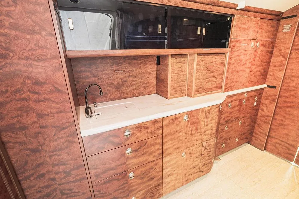 The aircraft galley area features a sink, white countertop, and extensive wood cabinetry with silver hardware.