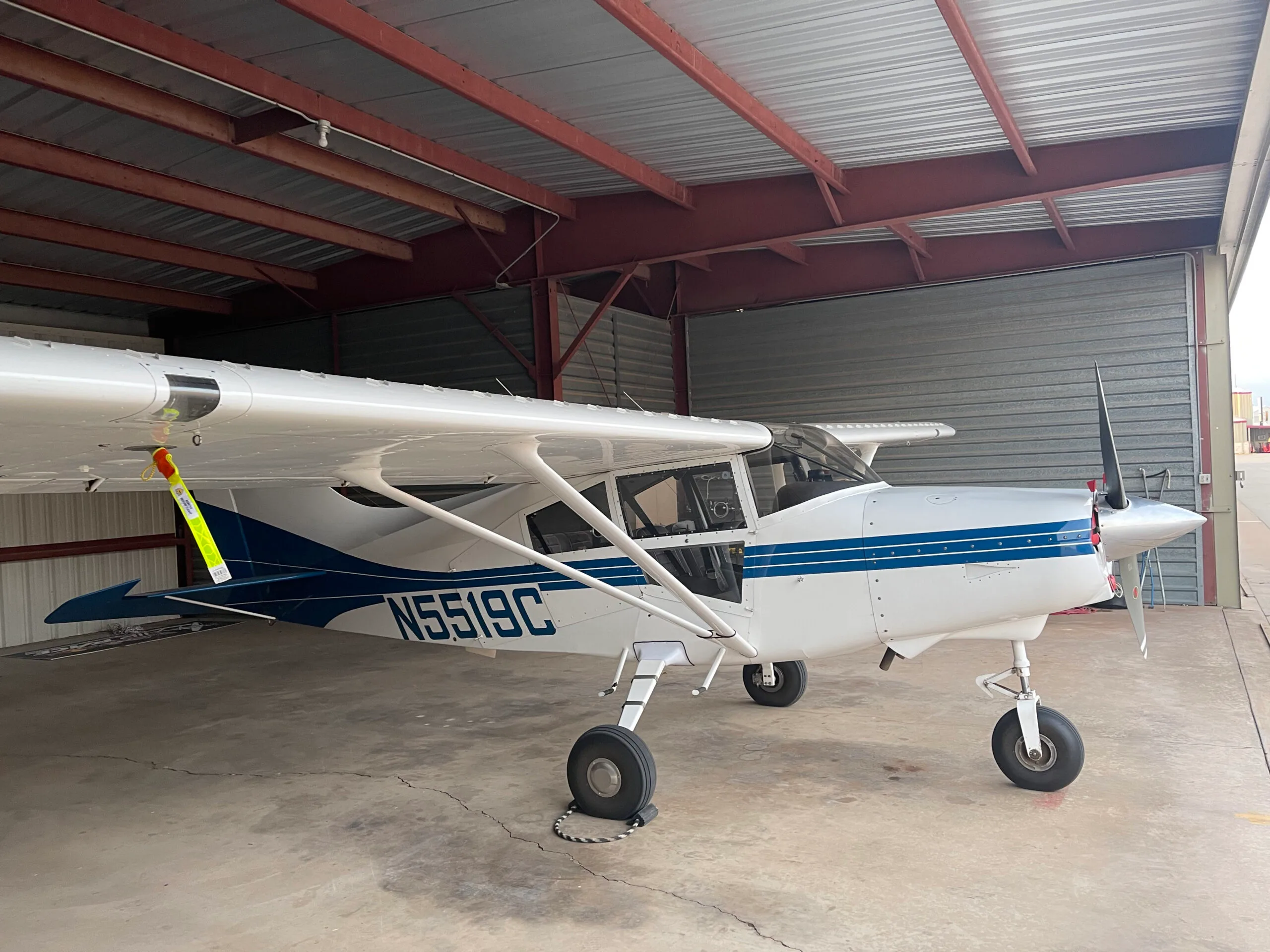 A white high-wing aircraft with blue stripes and registration N5519C is parked inside a hangar.