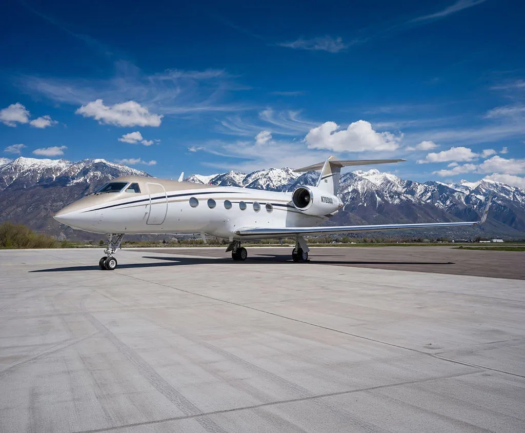 A white Gulfstream G650 business jet with registration N769MM is parked on an airfield with snow-capped mountains in the background.