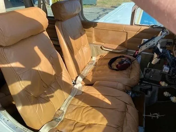The tan leather front seats of a small aircraft cabin, with a headset resting on the right seat.