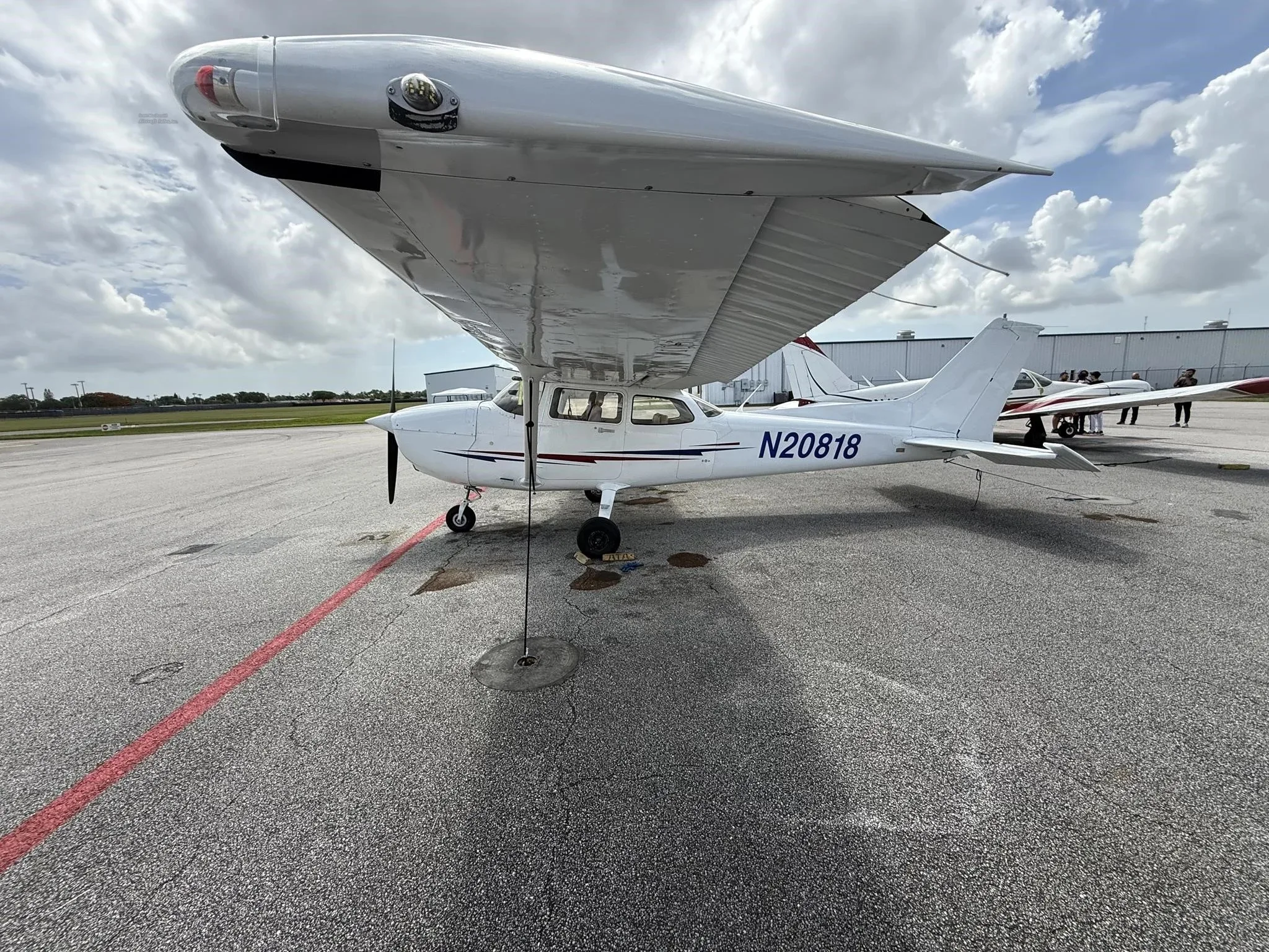 A white Cessna 172 (N20818) parked on an airport tarmac under a cloudy sky, viewed from the front-left.