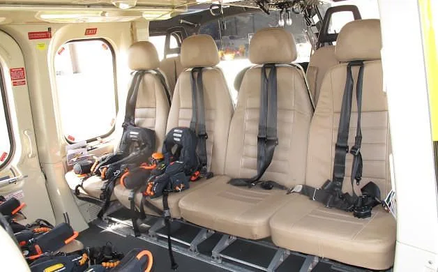 A close-up view of the beige passenger seats with safety harnesses inside a helicopter cabin.