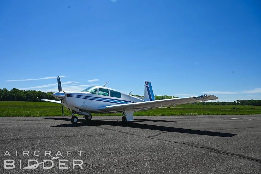 A white single-engine propeller aircraft with blue stripes is parked on an asphalt runway under a clear blue sky.