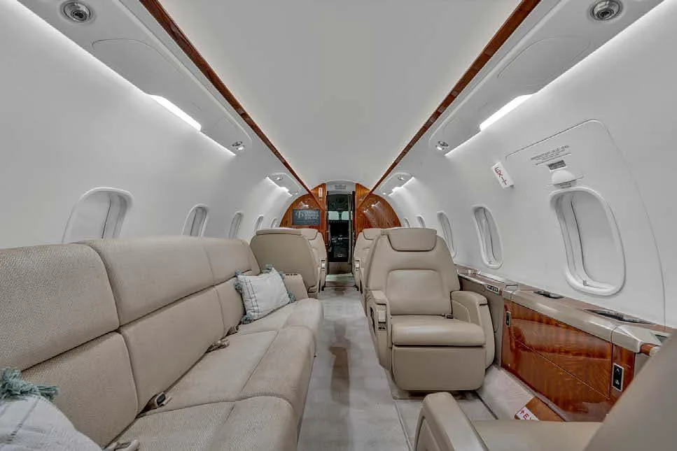 The aircraft cabin interior featuring a beige sofa, individual seats, and polished wood paneling.