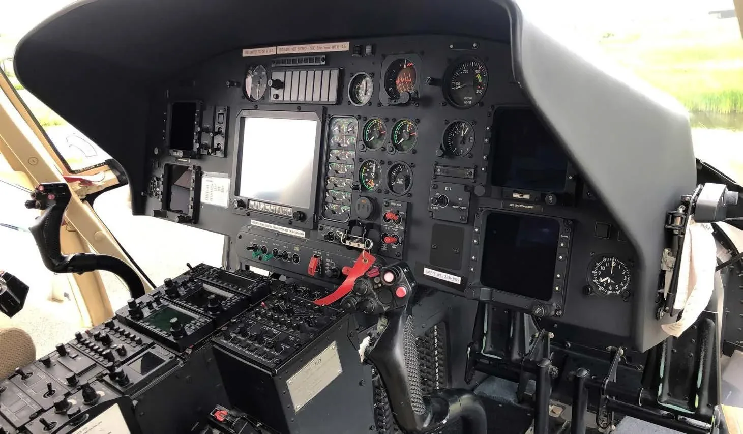 Detailed view of a helicopter's instrument panel with multiple gauges, screens, and flight controls.