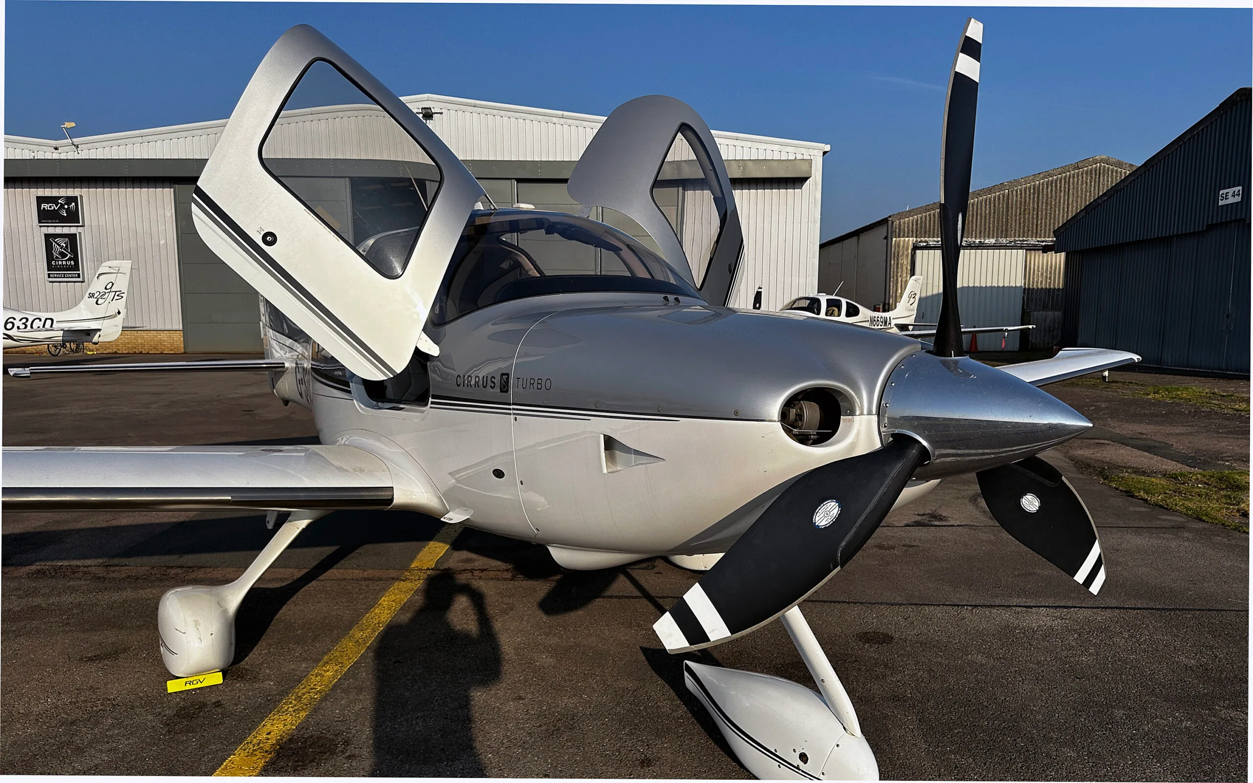 A silver and white Cirrus SR22 Turbo aircraft with its doors open, parked on an airfield.