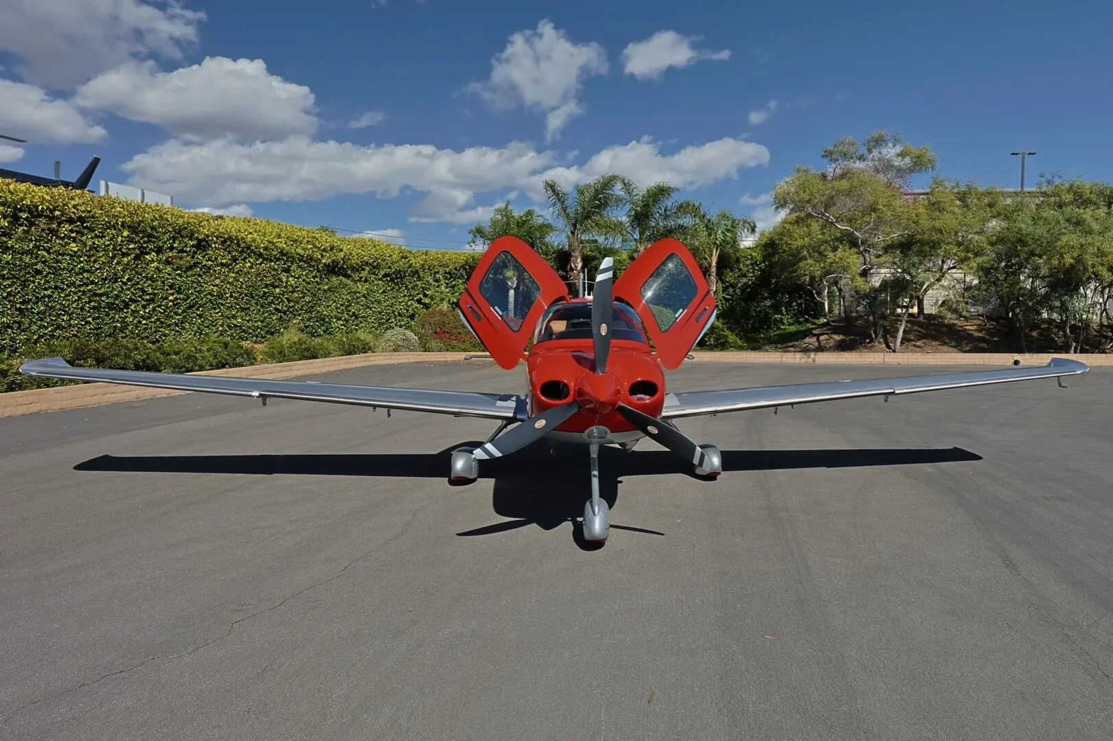 A front view of the red and silver Cirrus SR22 GTS aircraft, N245WP, with its gull-wing doors open.