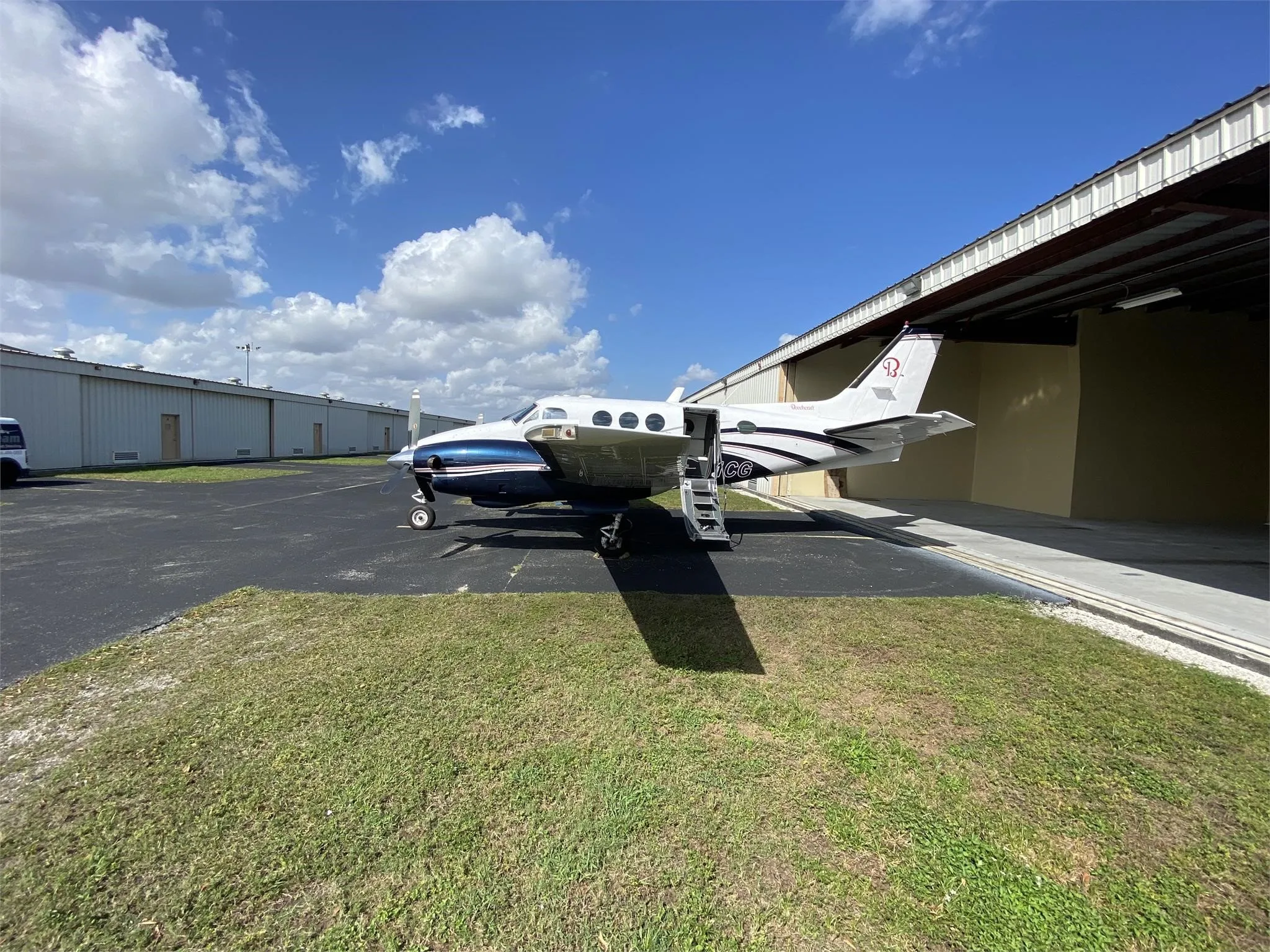 A side view of a white and dark blue Beechcraft King Air with its passenger door open and stairs extended, parked on an airfield.