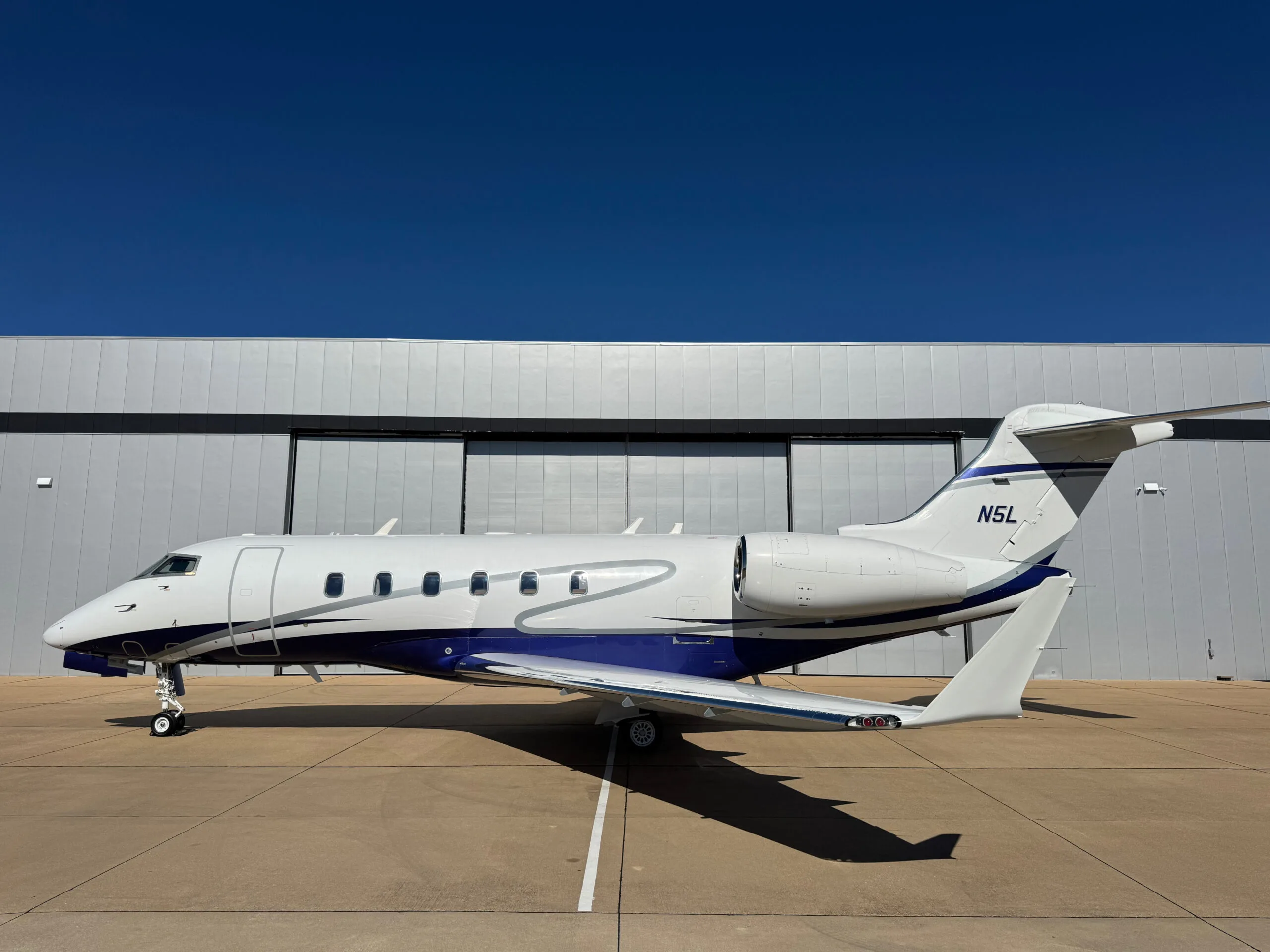 Side view of the N5L business jet, a white aircraft with blue and silver stripes, parked on an airfield.