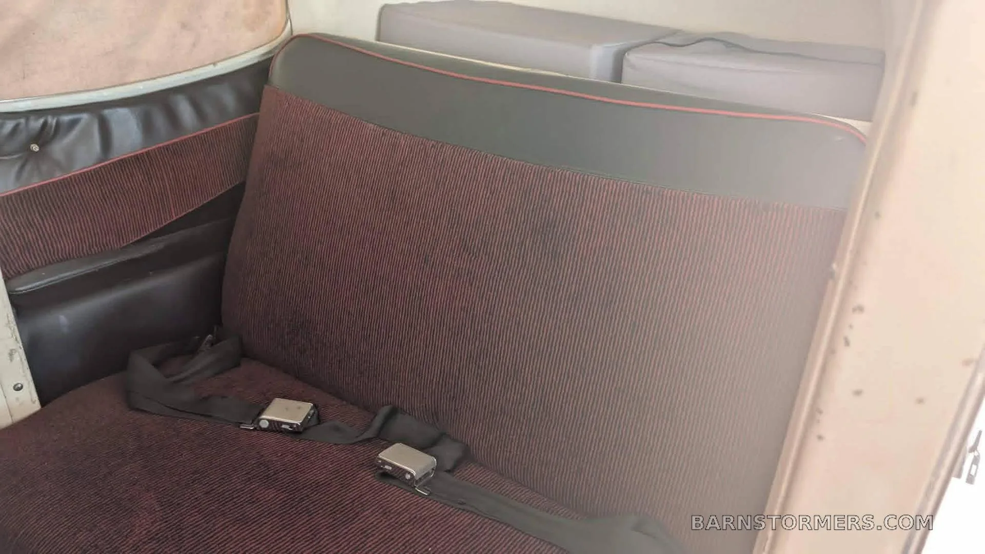 The rear passenger seats of an aircraft cabin, upholstered in red striped fabric with black trim.