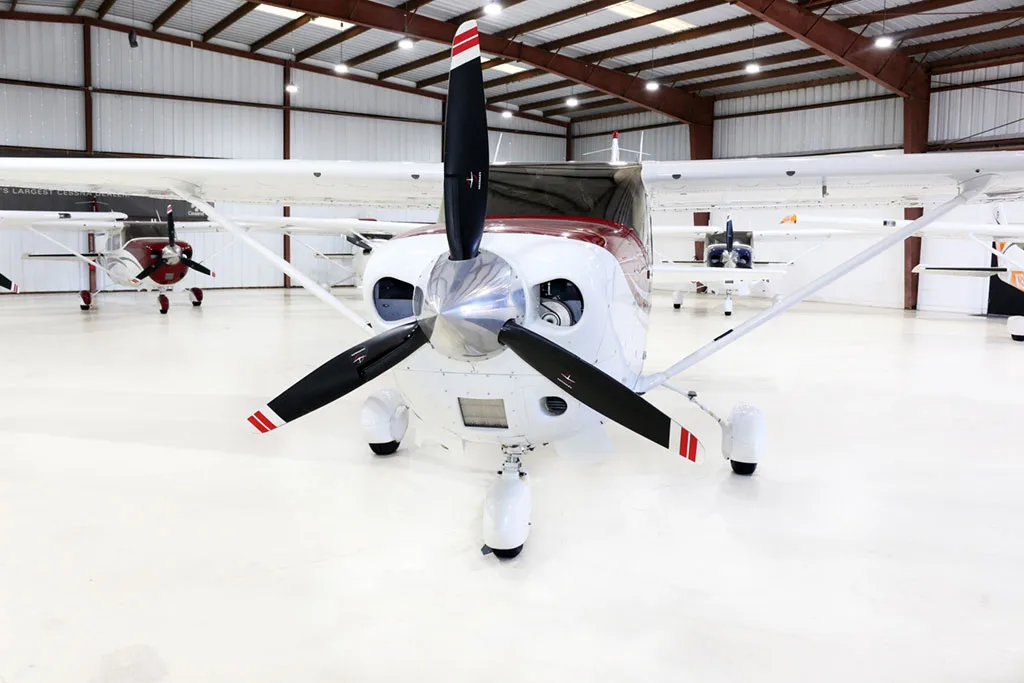 A white and red Cessna Stationair TC aircraft (N369CV) is parked head-on in a hangar, showing its propeller.