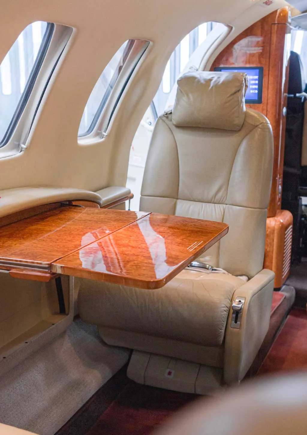 A close-up view of a beige leather cabin seat with a polished wooden fold-out table extended in front of it.