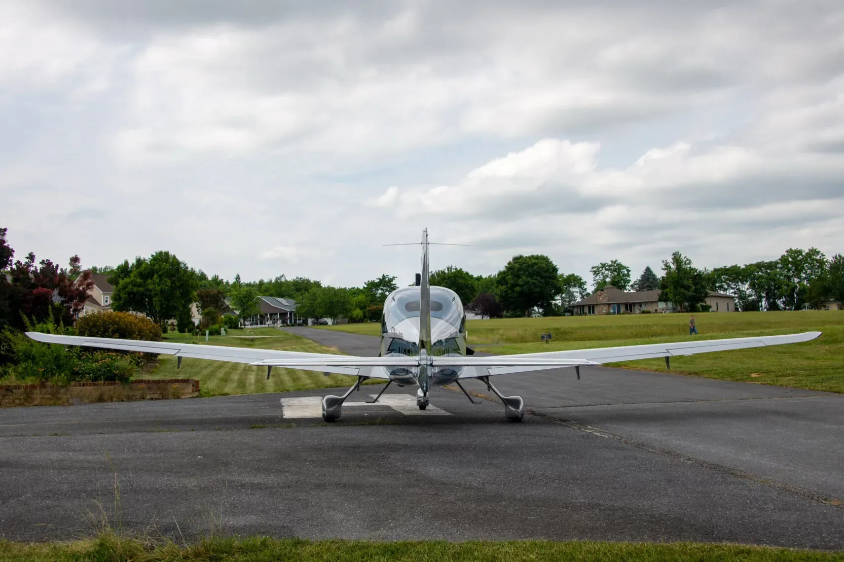 Rear view of a Cirrus SR22T Carbon aircraft, N27MY, on a runway with houses and trees in the background.