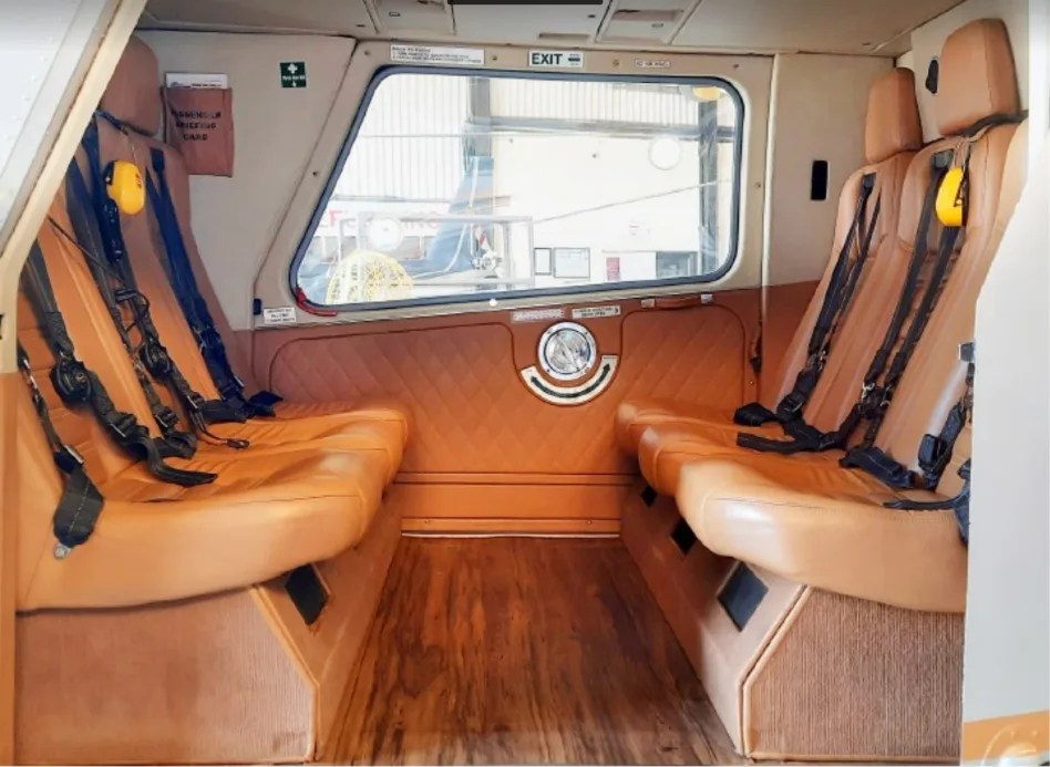 A wide view of a helicopter's interior cabin featuring tan leather seats, black seatbelts, and a wooden floor.