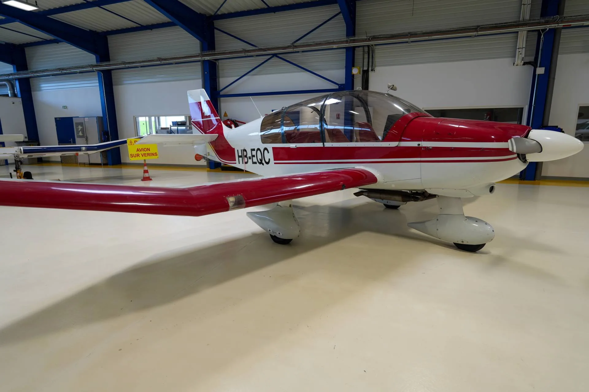 A red and white single-engine aircraft, registration HB-EQC, parked inside a hangar.