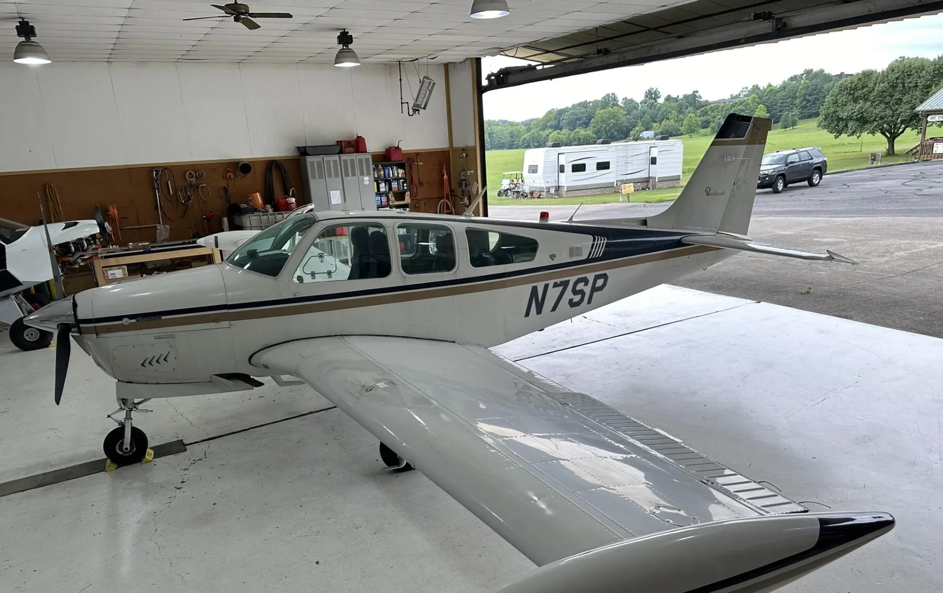 A white and gold Beechcraft Bonanza N7SP parked in a hangar, viewed from the rear right.