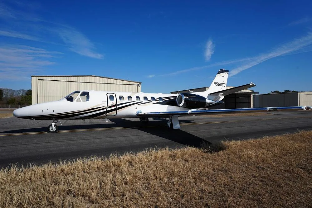 A side view of the white Cessna Citation Encore business jet N560CB with black and gold stripes, parked on an airfield.