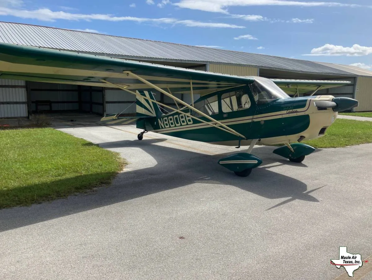 A green and cream Maule M-series aircraft, N8808N, parked on an asphalt ramp next to a hangar under a partly cloudy sky.